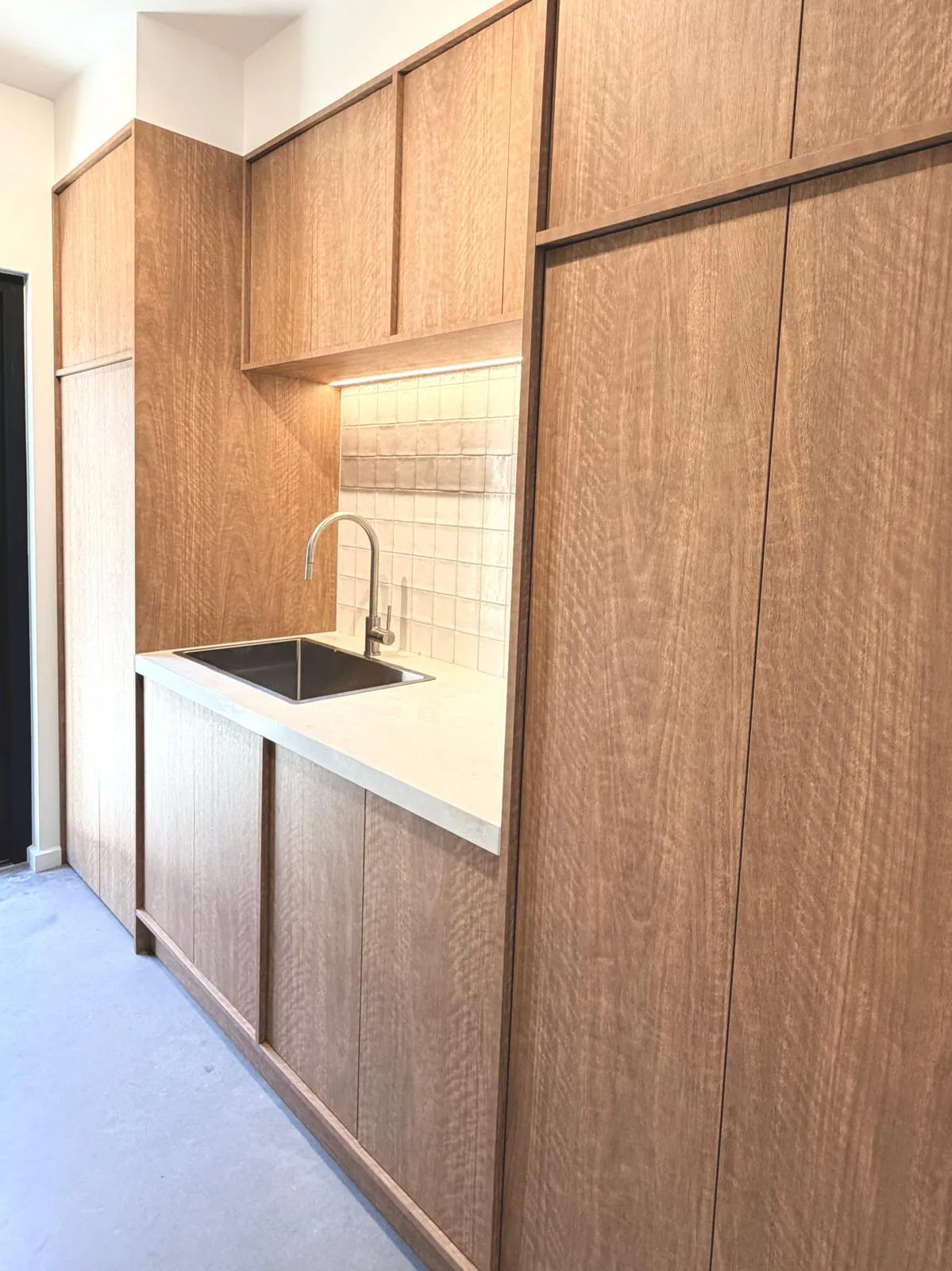Warm timber custom laundry cabinetry with integrated storage and a central sink